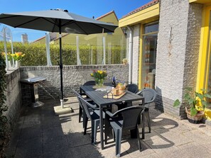An outdoor patio with a table, chairs, a grill, and a large umbrella.