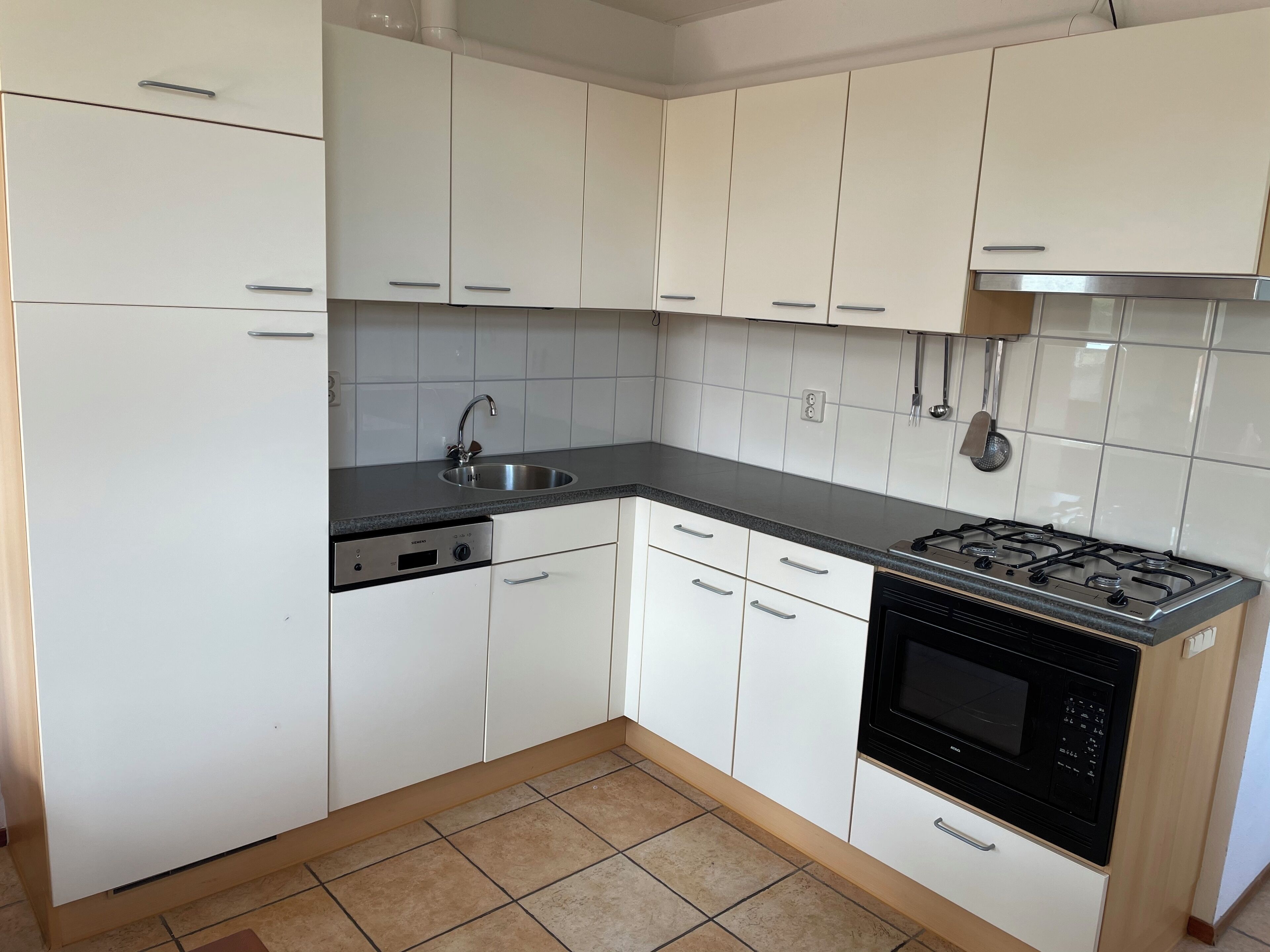 Een keuken met witte kastjes, een zwart aanrecht, een roestvrijstalen spoelbak, een vaatwasser en een zwart fornuis.