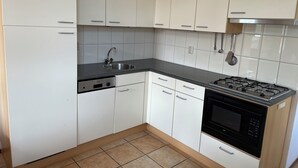 A kitchen with white cabinets, a black countertop, a stainless steel sink, a dishwasher, and a black stove. - 3 bedroom accommodation in Julianadorp aan Zee (Julianadorp aan Zee)