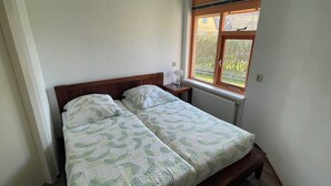 A small, clean bedroom with a single bed, a bedside table, a window with a view of greenery, and a radiator.