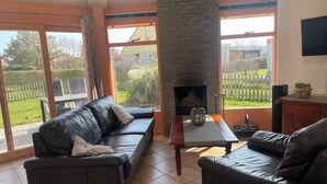 A living room with a fireplace, a black leather sofa, and a view of the outside.