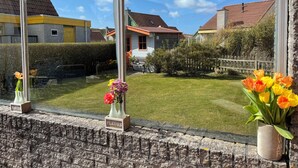 A view from a window overlooking a well-maintained garden with a wooden fence, a lawn, and houses in the background. - 2 bedroom accommodation in Julianadorp aan Zee (Julianadorp aan Zee)