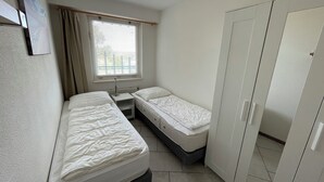 A small, clean room with two beds, a wardrobe, and a window with curtains.