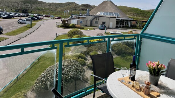 A balcony with a table set for dining, overlooking a parking area and a building with a distinctive conical roof.