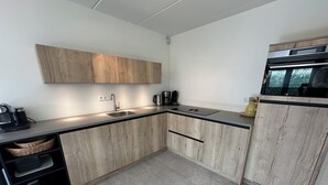 A modern kitchen with wooden cabinets, a black countertop, a stainless steel sink, and a built-in oven. - 3 bedroom accommodation in Julianadorp (Julianadorp)