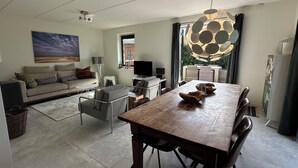 A modern living room with a wooden dining table, a sofa, and a TV. - 3 bedroom accommodation in Julianadorp (Julianadorp)