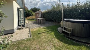 A backyard with a hot tub, a small wooden structure, and a patio area. - 3 bedroom accommodation in Julianadorp (Julianadorp)