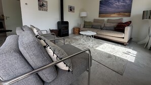 A modern living room with a sofa, a coffee table, a fireplace, and a painting on the wall. - 3 bedroom accommodation in Julianadorp (Julianadorp)