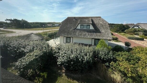 A house with a thatched roof, surrounded by lush greenery and a clear sky. - 3 bedroom accommodation in Julianadorp (Julianadorp)