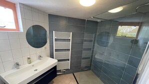 Un bagno con lavandino bianco, piastrelle scure, uno specchio e zona doccia.