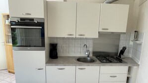 Una cucina compatta con forno, piano cottura a gas, lavello e macchina per il caffè.
