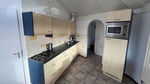 A compact kitchen with light wooden cabinets, a black countertop, a built-in microwave, and a tiled floor. - 3 bedroom accommodation in Julianadorp aan Zee (Julianadorp aan Zee)