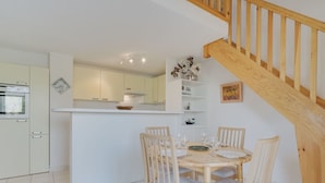 Een moderne keuken met witte kasten, een houten eettafel met vier stoelen en een trap met houten leuningen.
