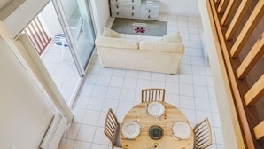Een moderne woonkamer met een ronde houten eettafel voor vier personen, een bank en een televisie aan de muur.
