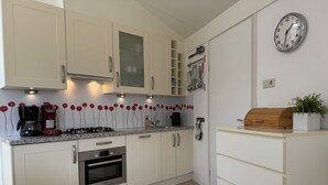 Eine moderne Küche mit weißen Schränken, einem Bosch-Ofen, einer Kaffeemaschine und einer Uhr an der Wand.