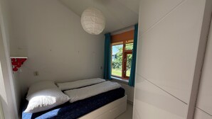 Ein kleiner, kompakter Raum mit Bett, einem Fenster mit Vorhängen und einer weißen Deckenleuchte.