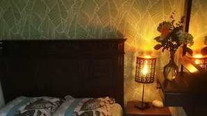 Un dormitorio con una cama, una mesita de noche, una lámpara y un florero con flores.