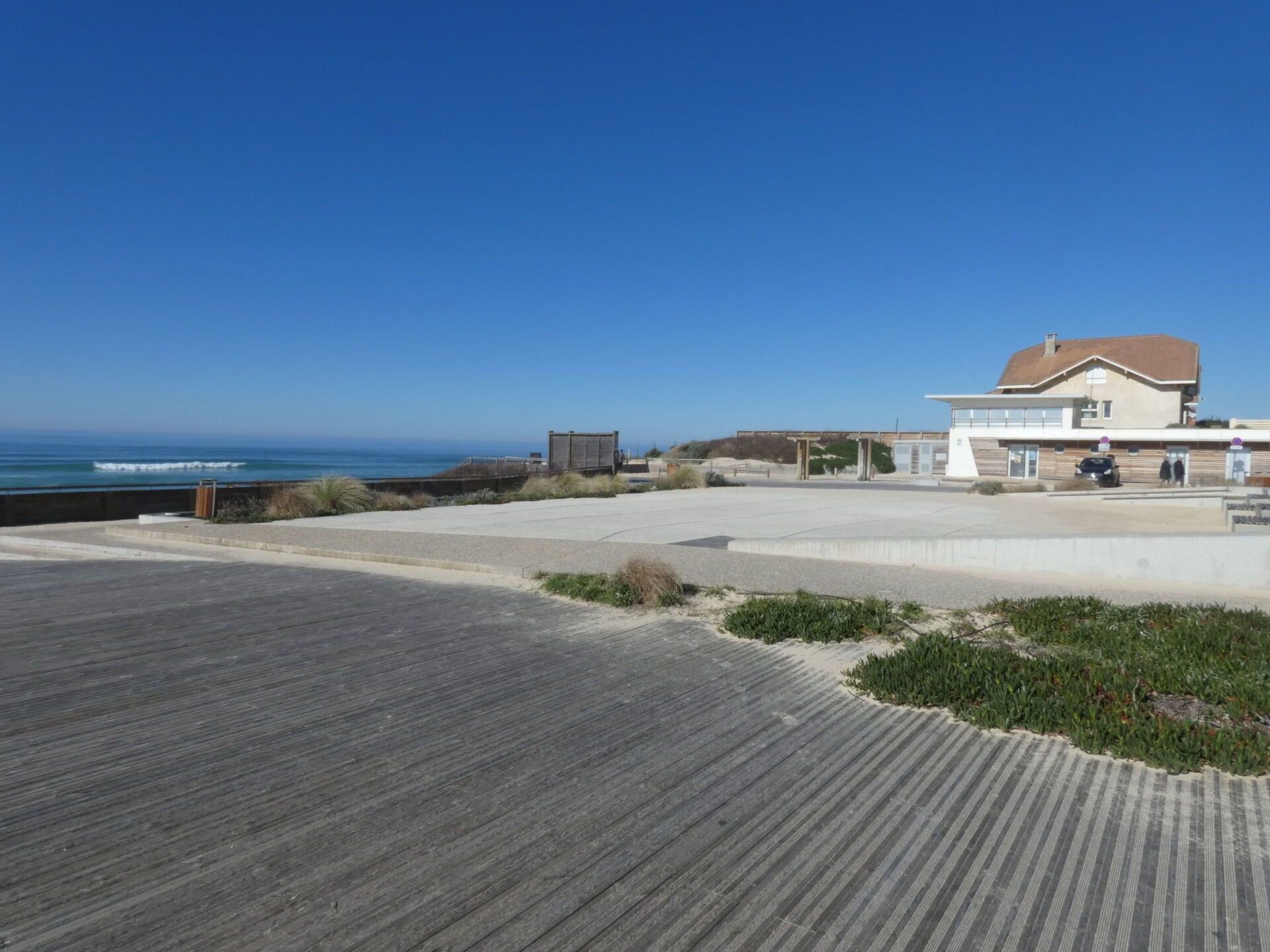 A beachfront property with a wooden deck, a building with a red roof, and a clear view of the ocean.