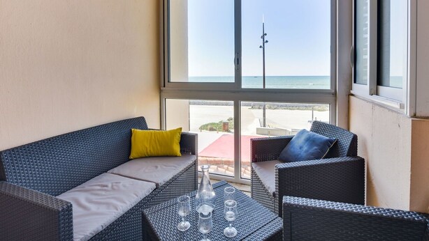 En balkon med fletmøbler, et glasbord og udsigt over stranden og havet.