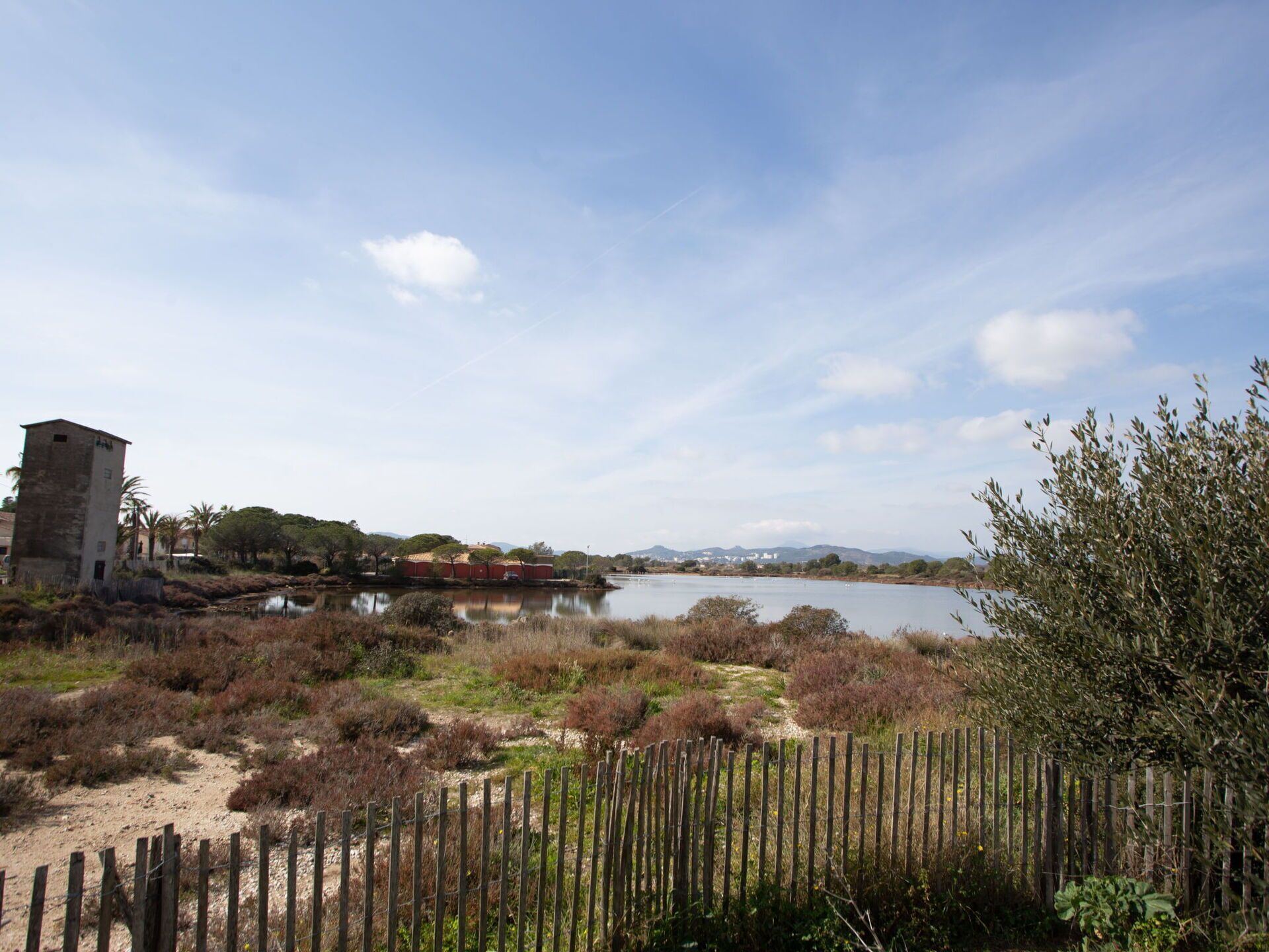 A natural landscape with a body of water, a wooden fence, and a small building.