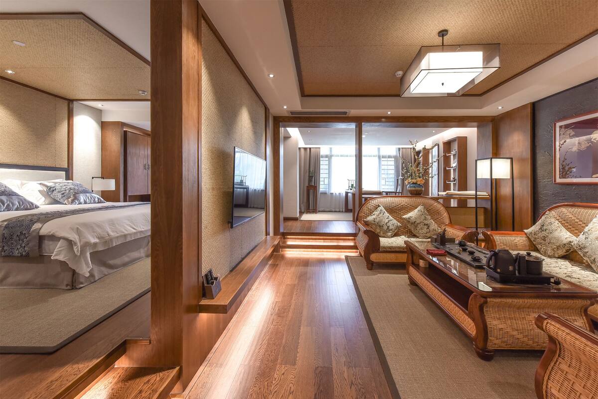 A modern hotel room with a bed, sofa, and a dining area.