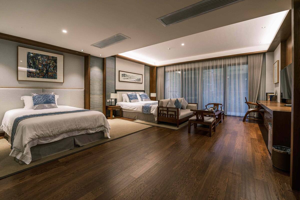 A modern hotel room with a large bed, a sofa, a desk, and a TV.