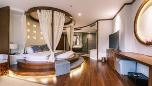 A modern hotel room with a curved bed, a TV, a bathroom, and a round mirror. - Yangshuo Mountain River Ballad Hotel (Guilin)