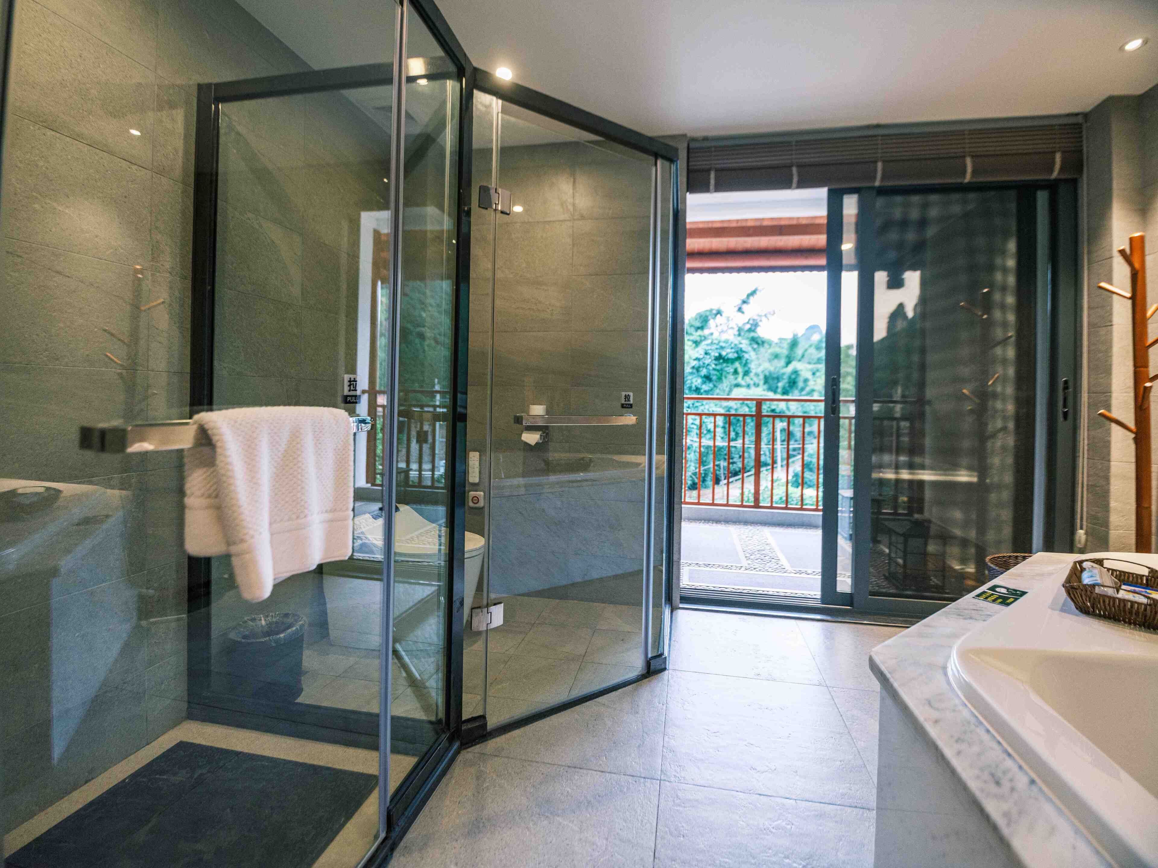 A modern bathroom with a glass shower enclosure, a large bathtub, and a balcony with a red railing.
