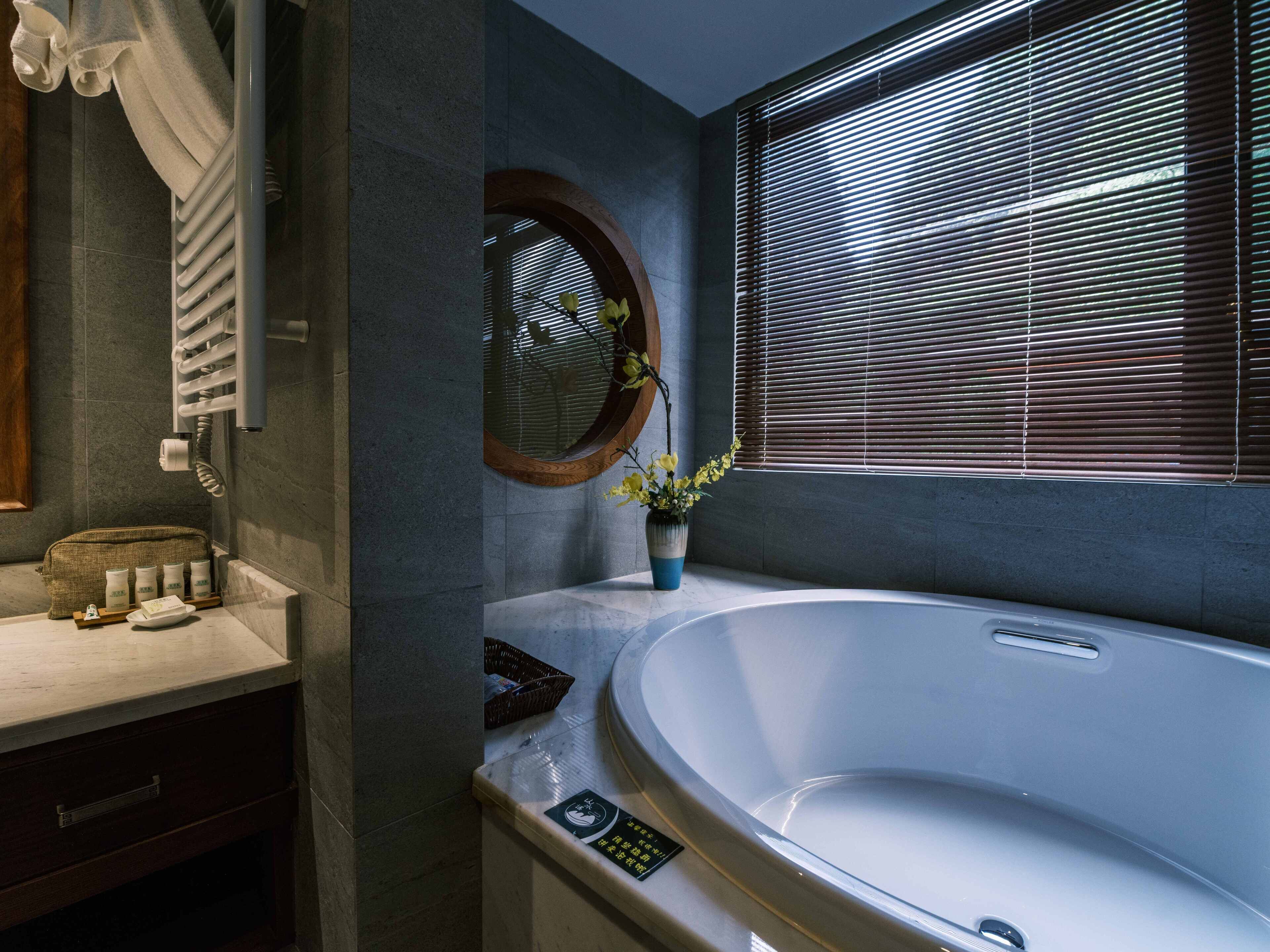 Un ba ño moderno con una bañera independiente, un tocador con espejo y una ventana con persianas.