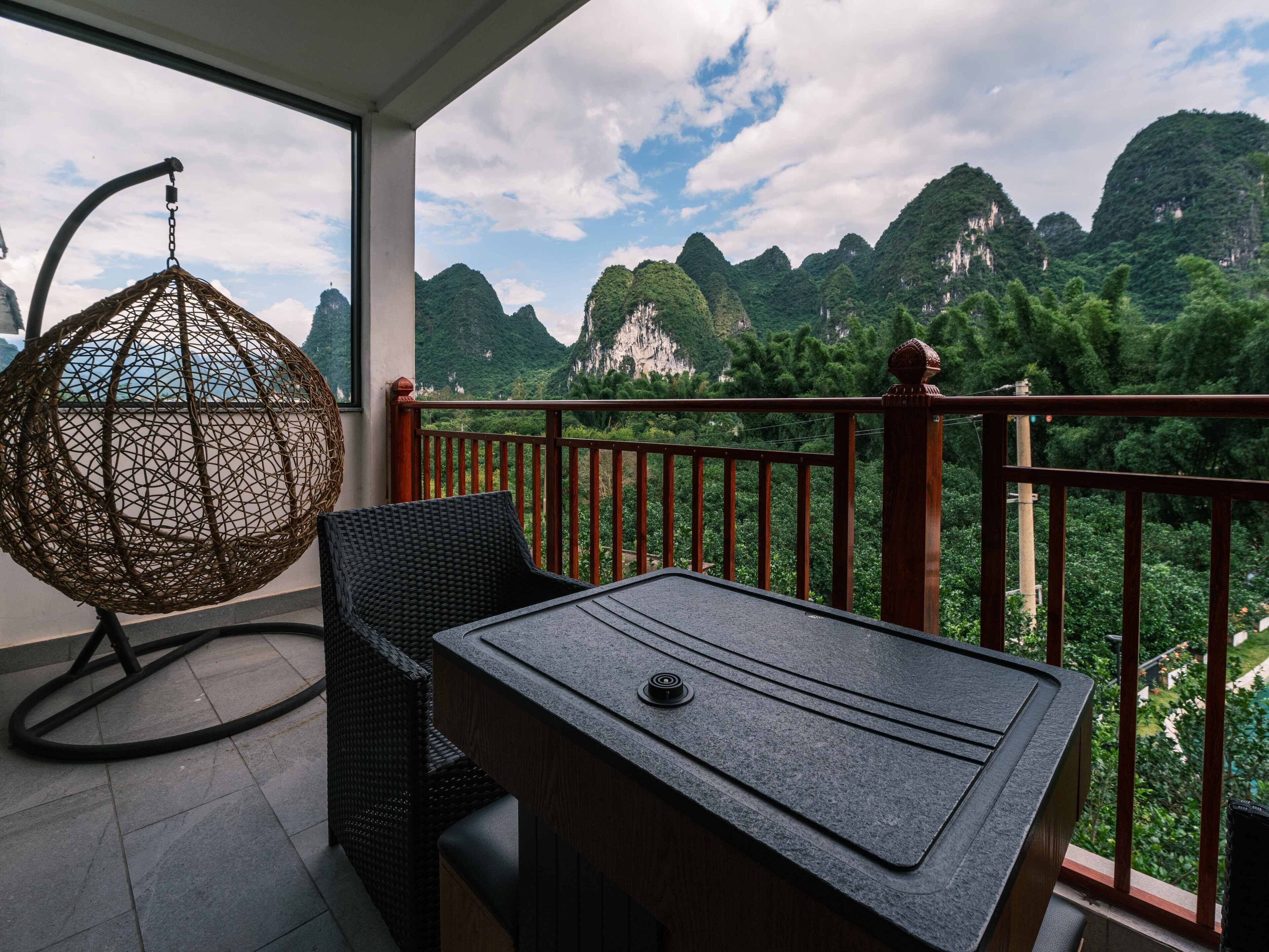 A balcony with a wicker chair and a table, overlooking a mountainous landscape.