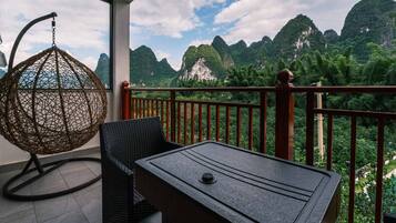 A balcony with a wicker chair and a table, overlooking a mountainous landscape.