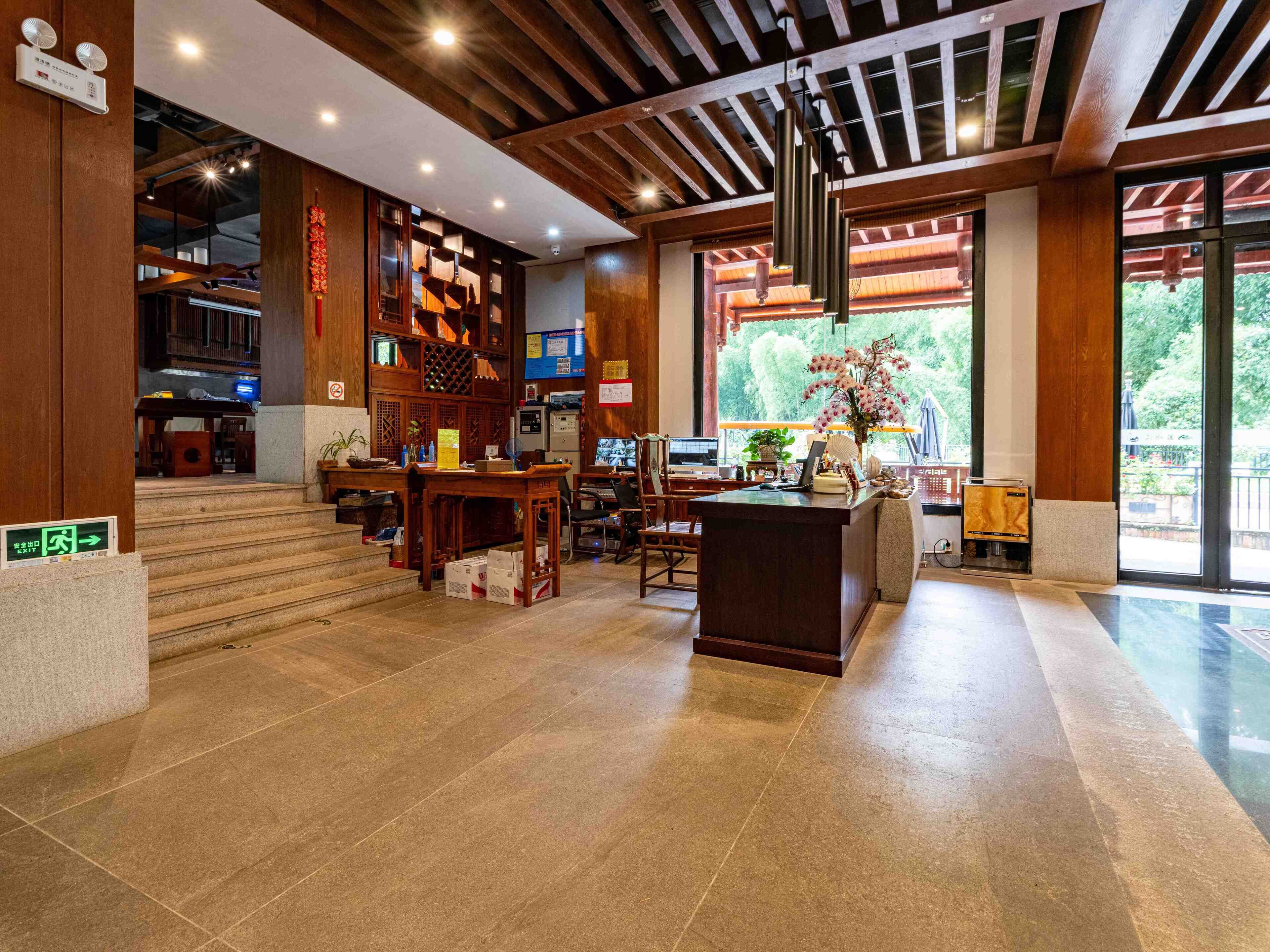 A lobby with a reception desk, wooden paneling, a staircase, and a large window with a view of greenery.