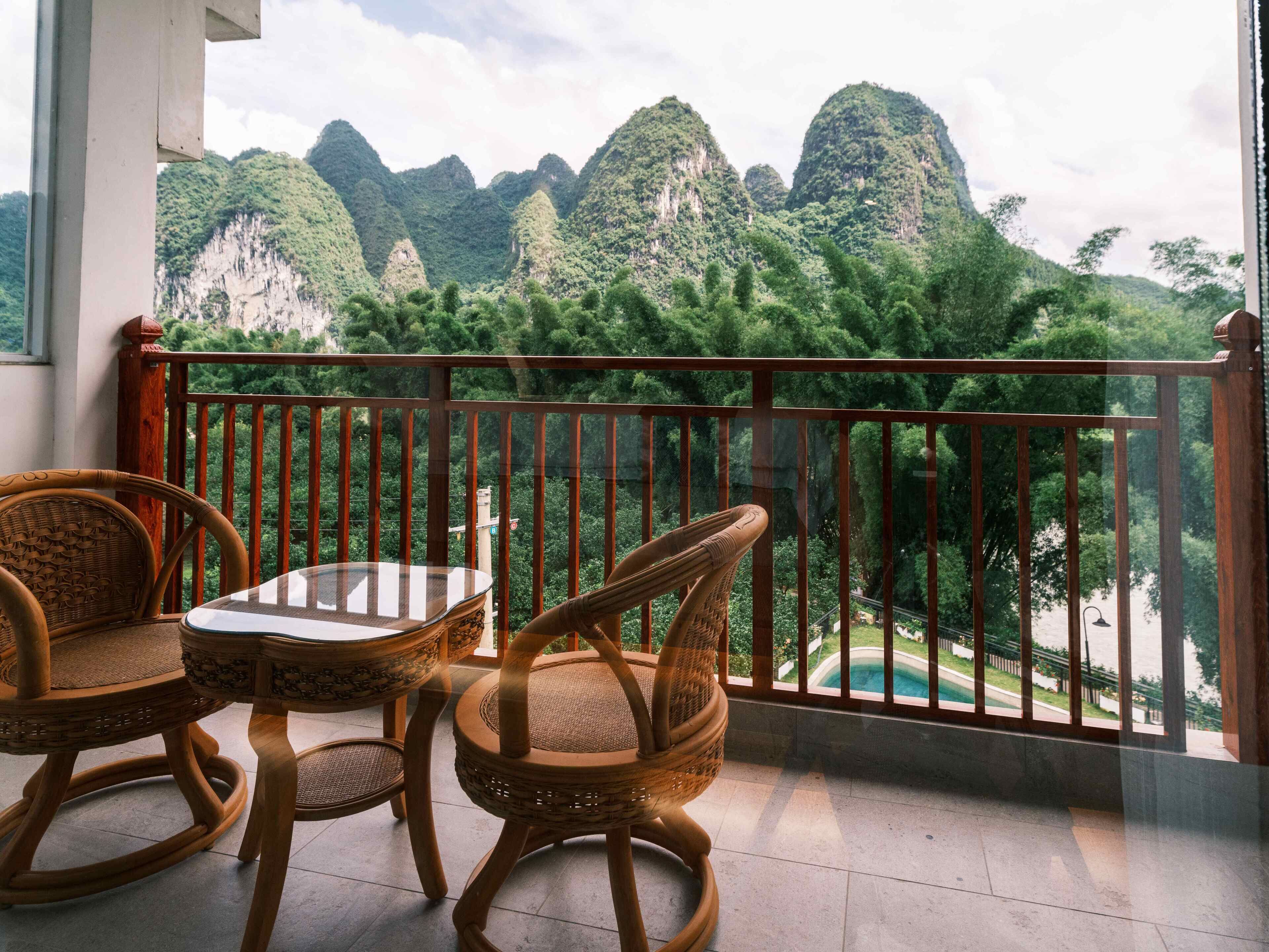 A balcony with wicker furniture and a glass table, overlooking a mountainous landscape.