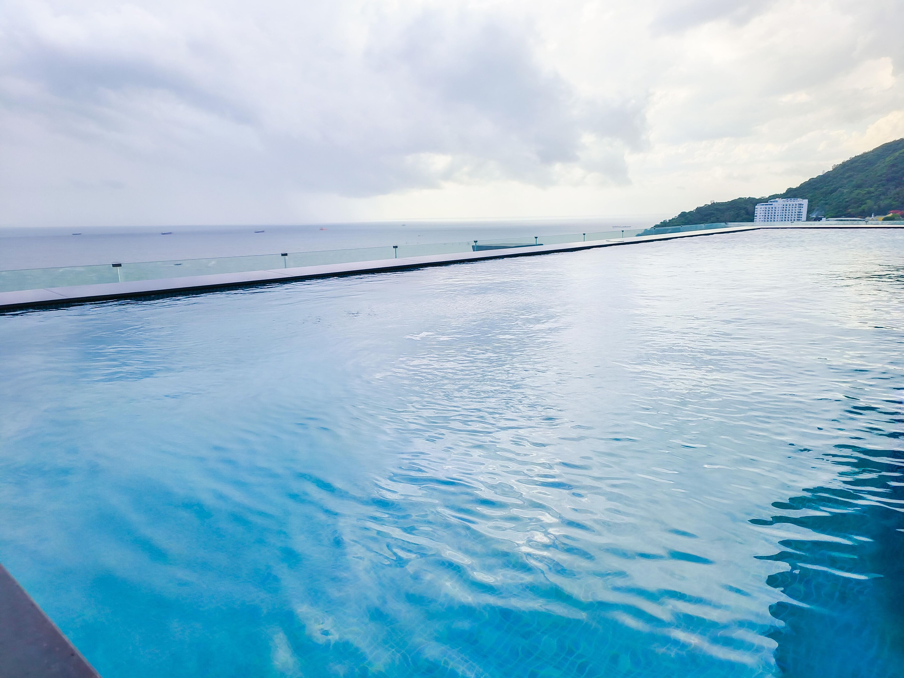 A swimming pool with clear blue water, a glass barrier, and a view of the ocean and a distant building.