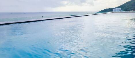 A swimming pool with clear blue water, a glass barrier, and a view of the ocean and a distant building.