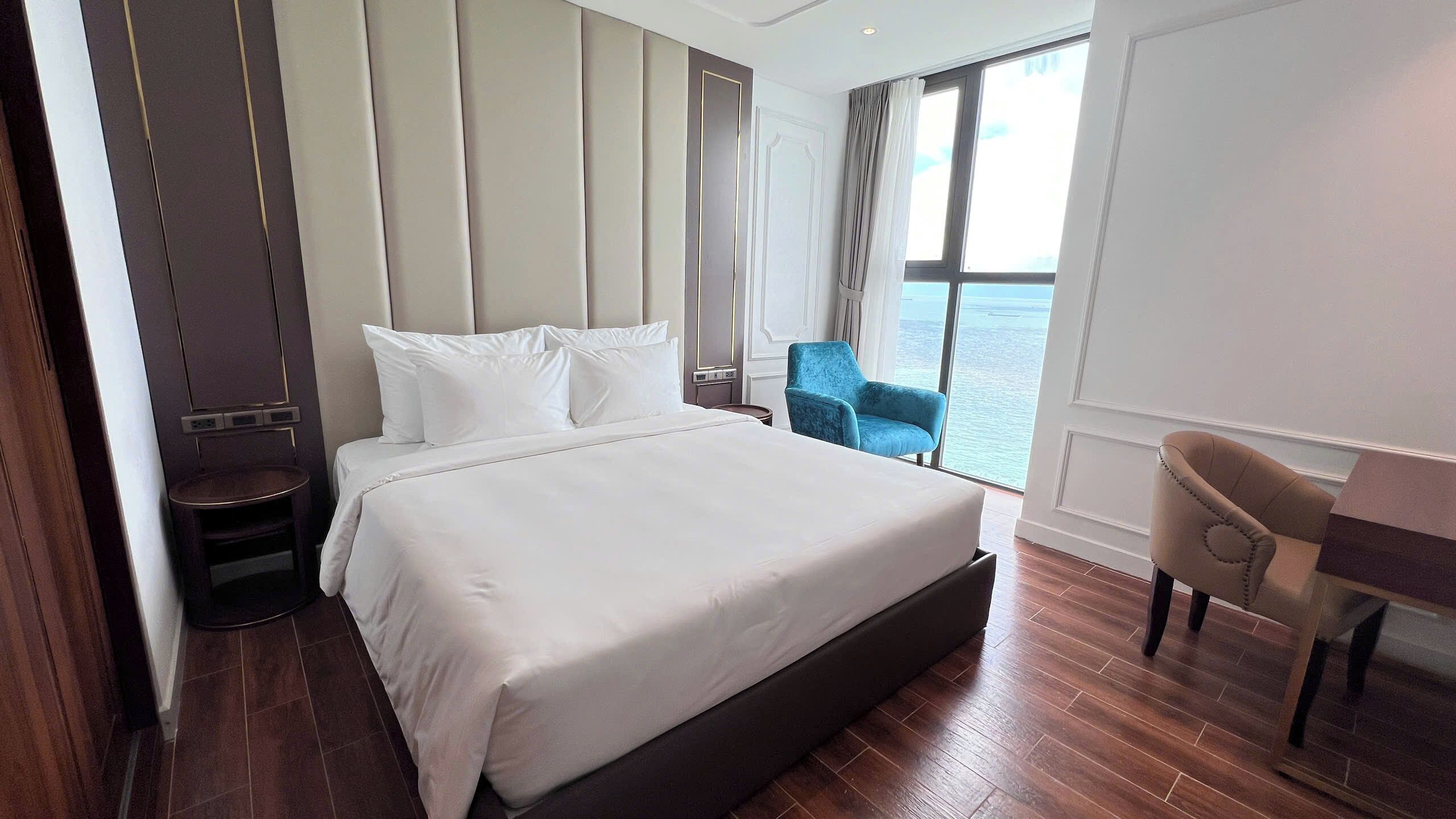 Une chambre d’hôtel avec un grand lit, un bureau, une chaise et une vue sur la mer.