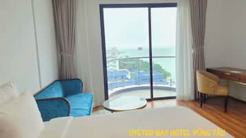 A hotel room with a bed, a blue sofa, a desk, and a view of the sea.