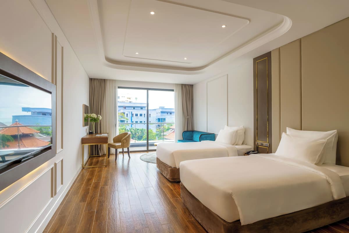 Une chambre d’hôtel avec une grande fenêtre, deux lits, un bureau et une chaise.