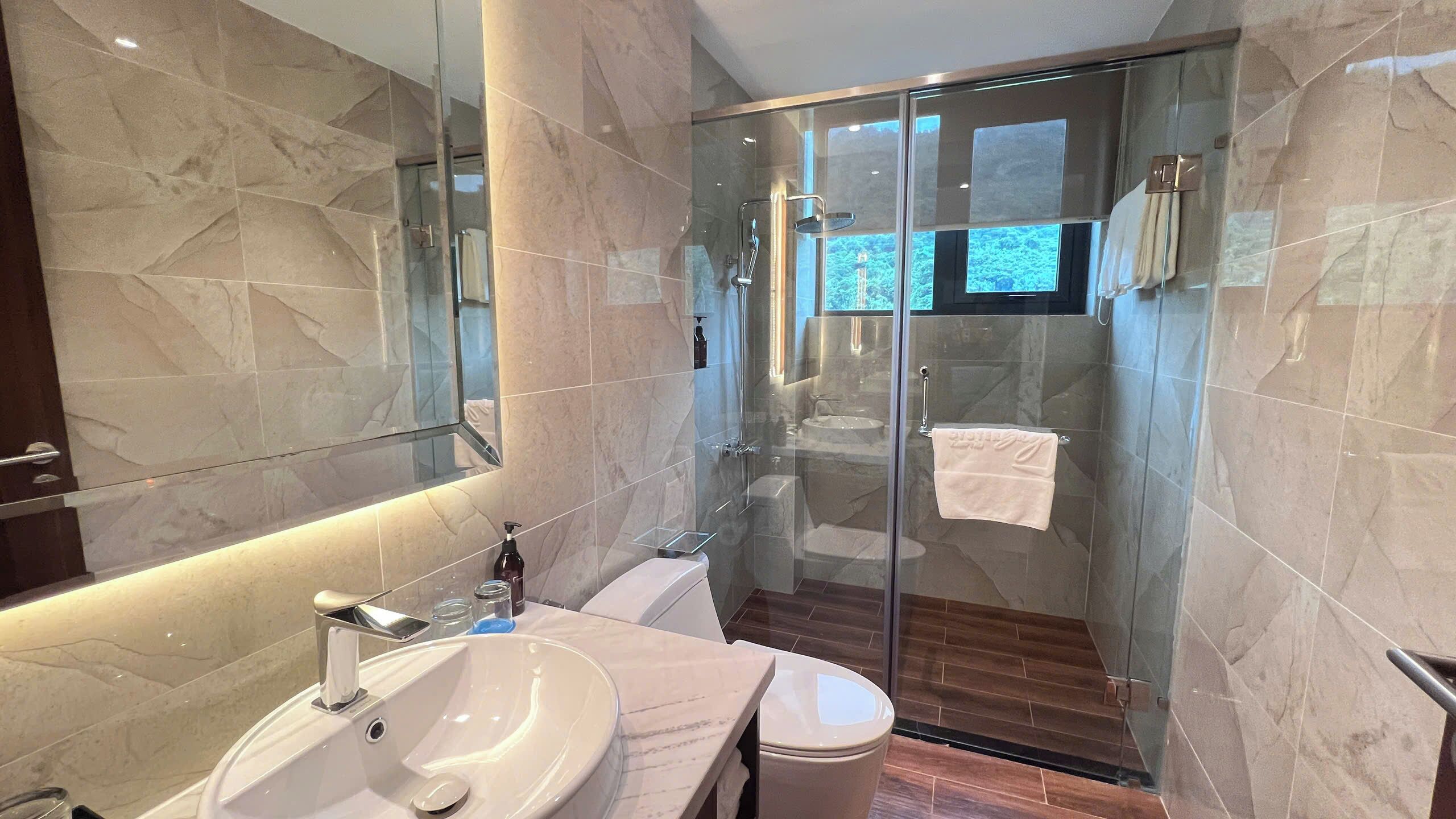 A modern bathroom with a glass-enclosed shower, a large mirror, and a marble-tiled wall.
