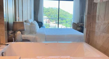 A hotel room with a large bed, a bathtub, and a view of a green hillside.