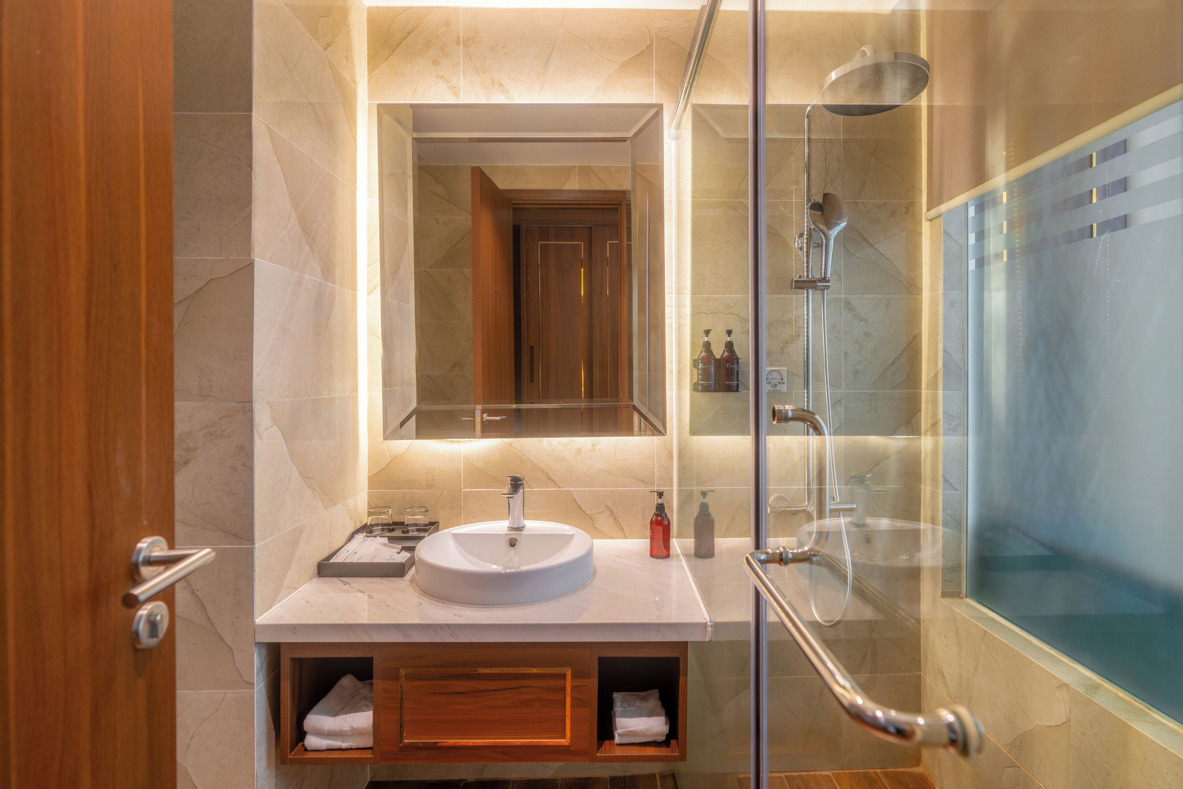A modern bathroom with a glass shower enclosure, a sink with a mirror above, and a wooden vanity with storage.