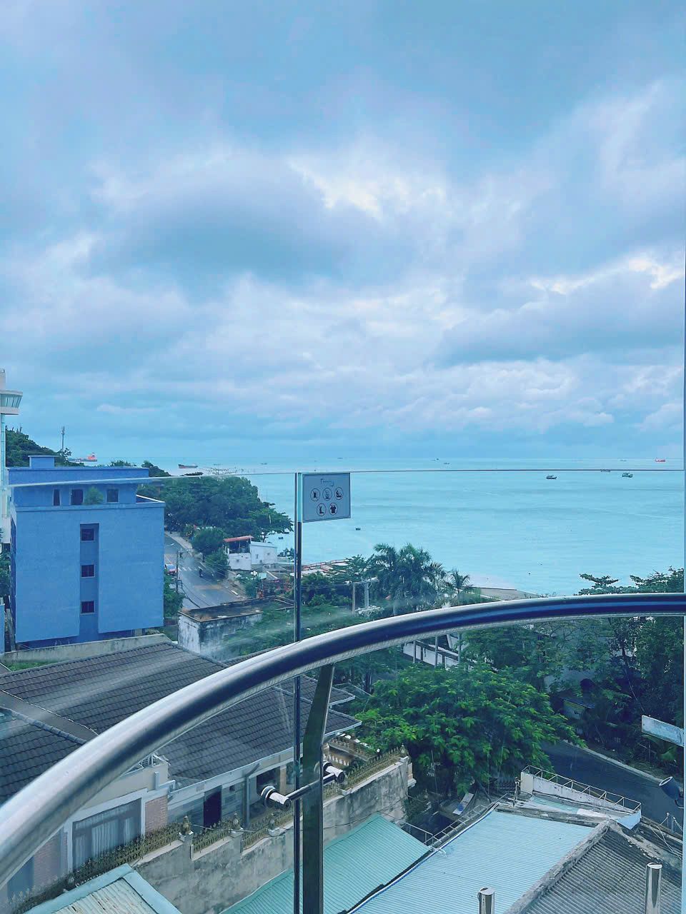 A coastal view from a balcony with a clear sky, a sign with symbols, and a distant body of water.