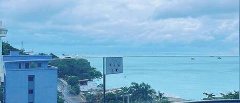 A coastal view from a balcony with a clear sky, a sign with symbols, and a distant body of water.