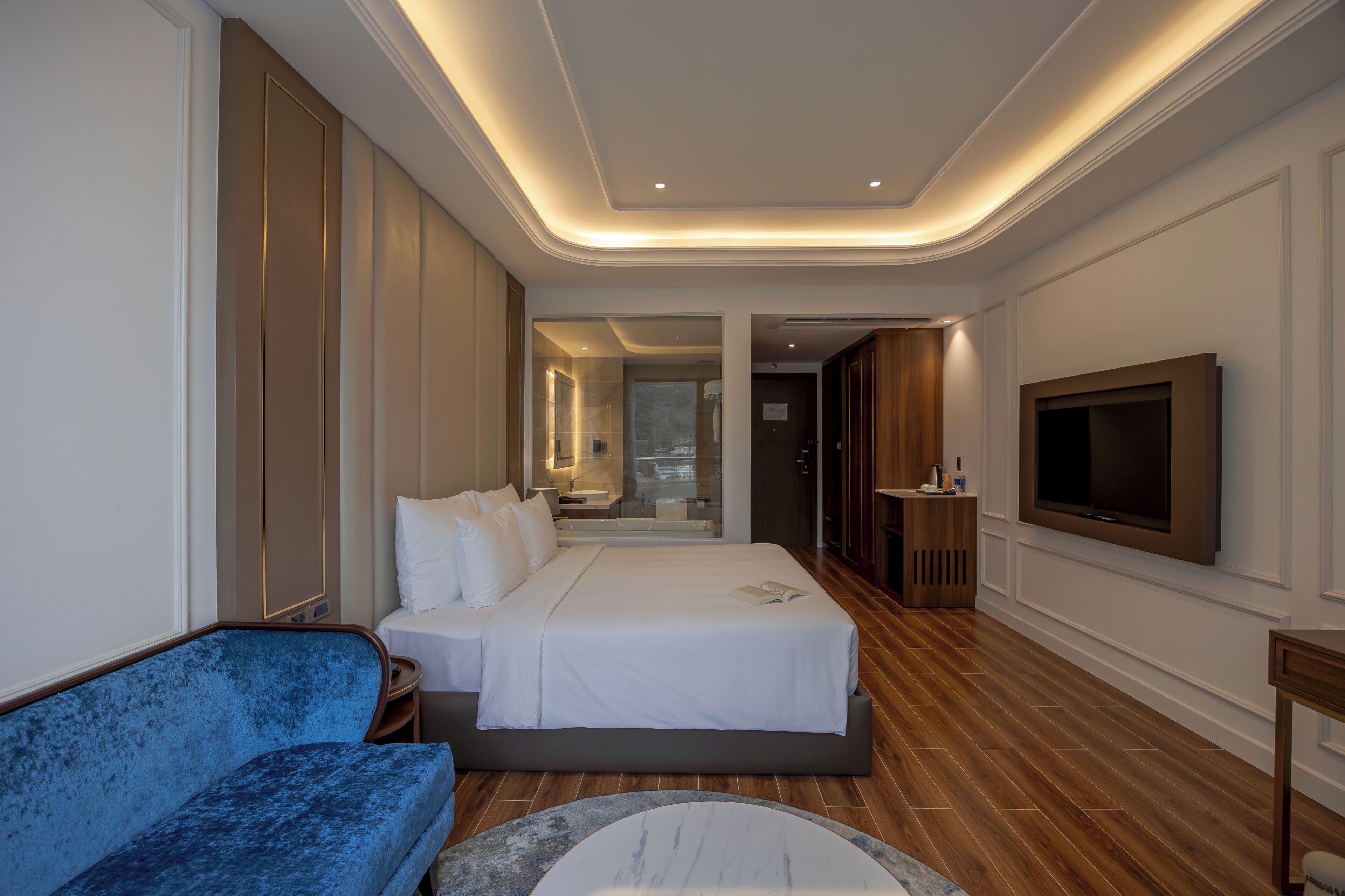 A modern hotel room with a large bed, a blue sofa, a TV, and a wooden floor.