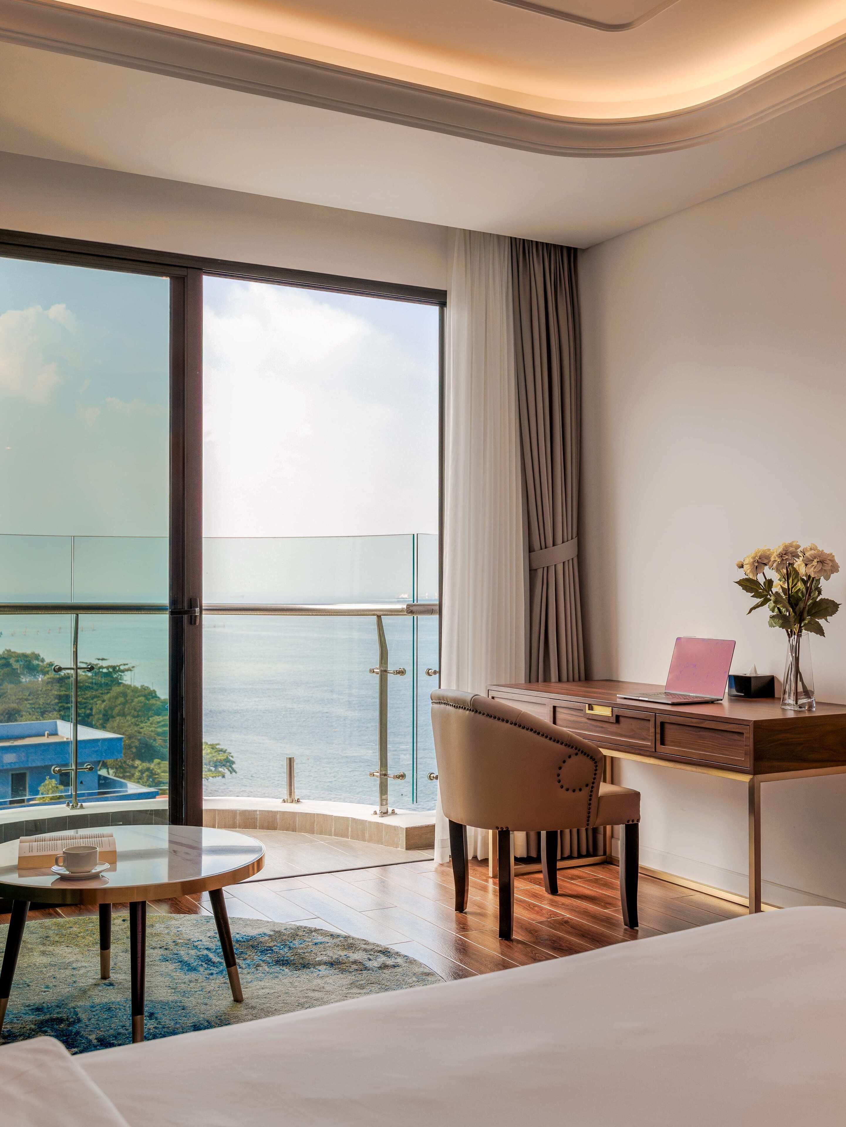 A hotel room with a large balcony, a desk with a laptop, a chair, and a bed.