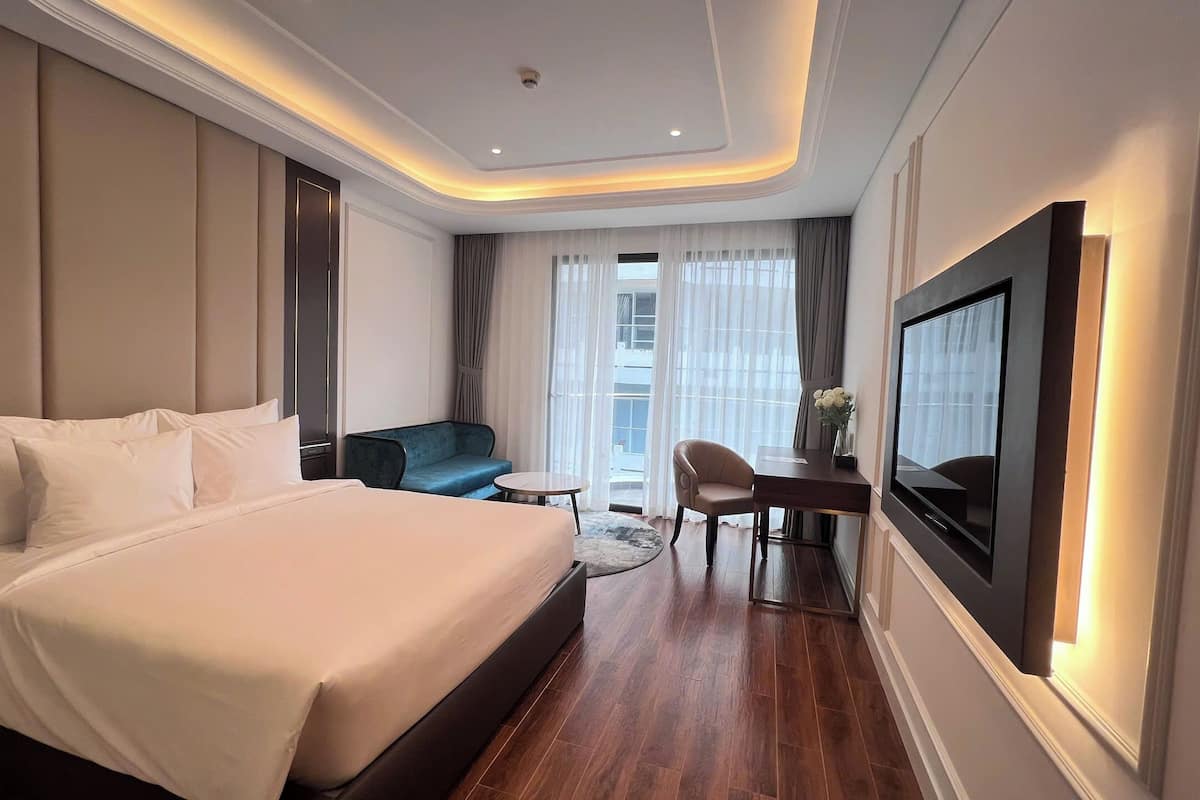 Une chambre d’hôtel moderne, dotée d’un grand lit, d’un bureau avec une chaise, d’un canapé et d’un téléviseur fixé au mur.