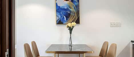 Un comedor con una mesa rectangular, cuatro sillas, un florero con flores, una lámpara en el techo y un cuadro colgado en la pared.