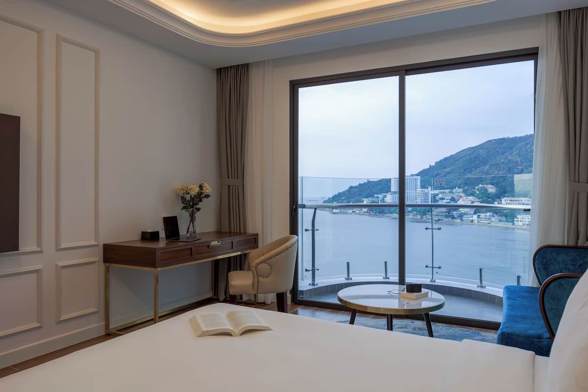 Une chambre d’hôtel avec une grande fenêtre, un lit, un bureau et une chaise.