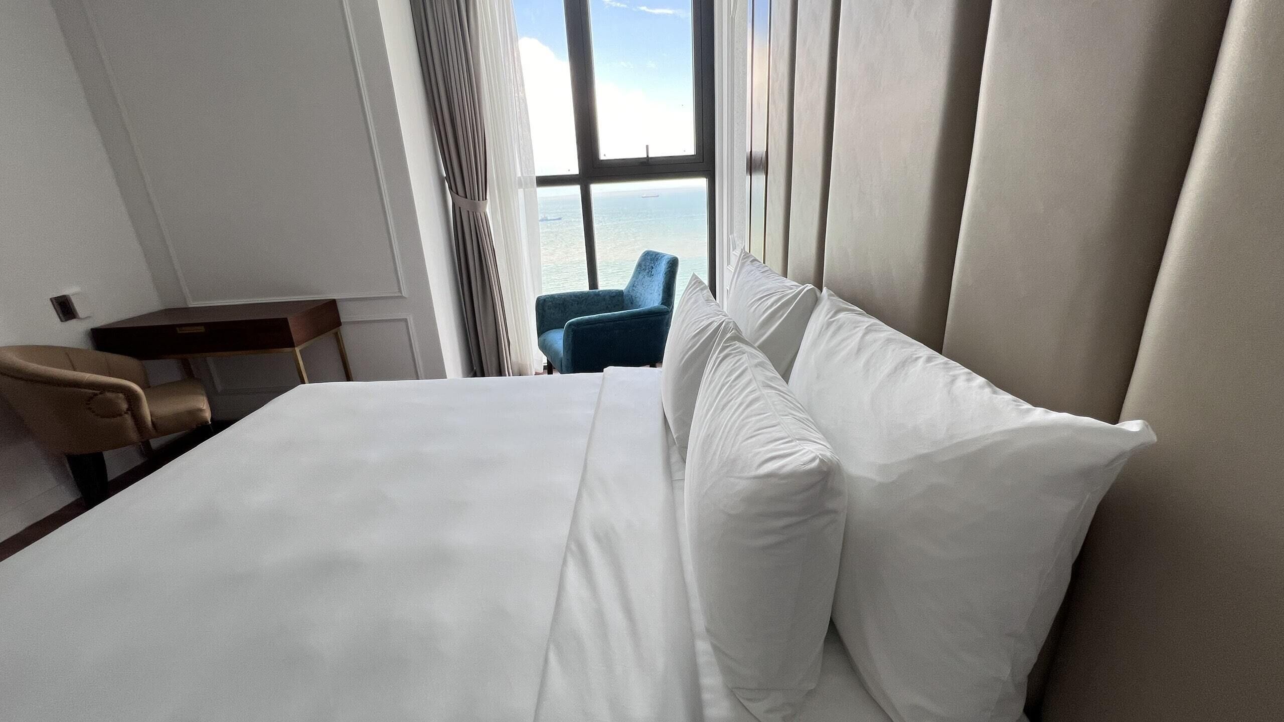 Habitación de hotel con una cama grande, un escritorio, una silla y vista al mar por la ventana.