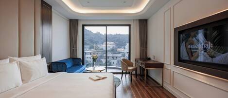 A hotel room with a large bed, a desk, a chair, a TV, and a view of a cityscape through a large window.